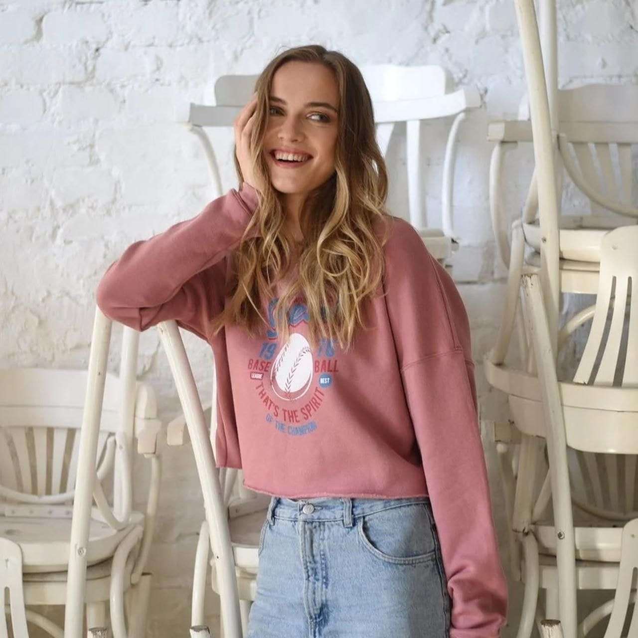 A smiling woman in a pink hoodie with a sport-themed chest print.